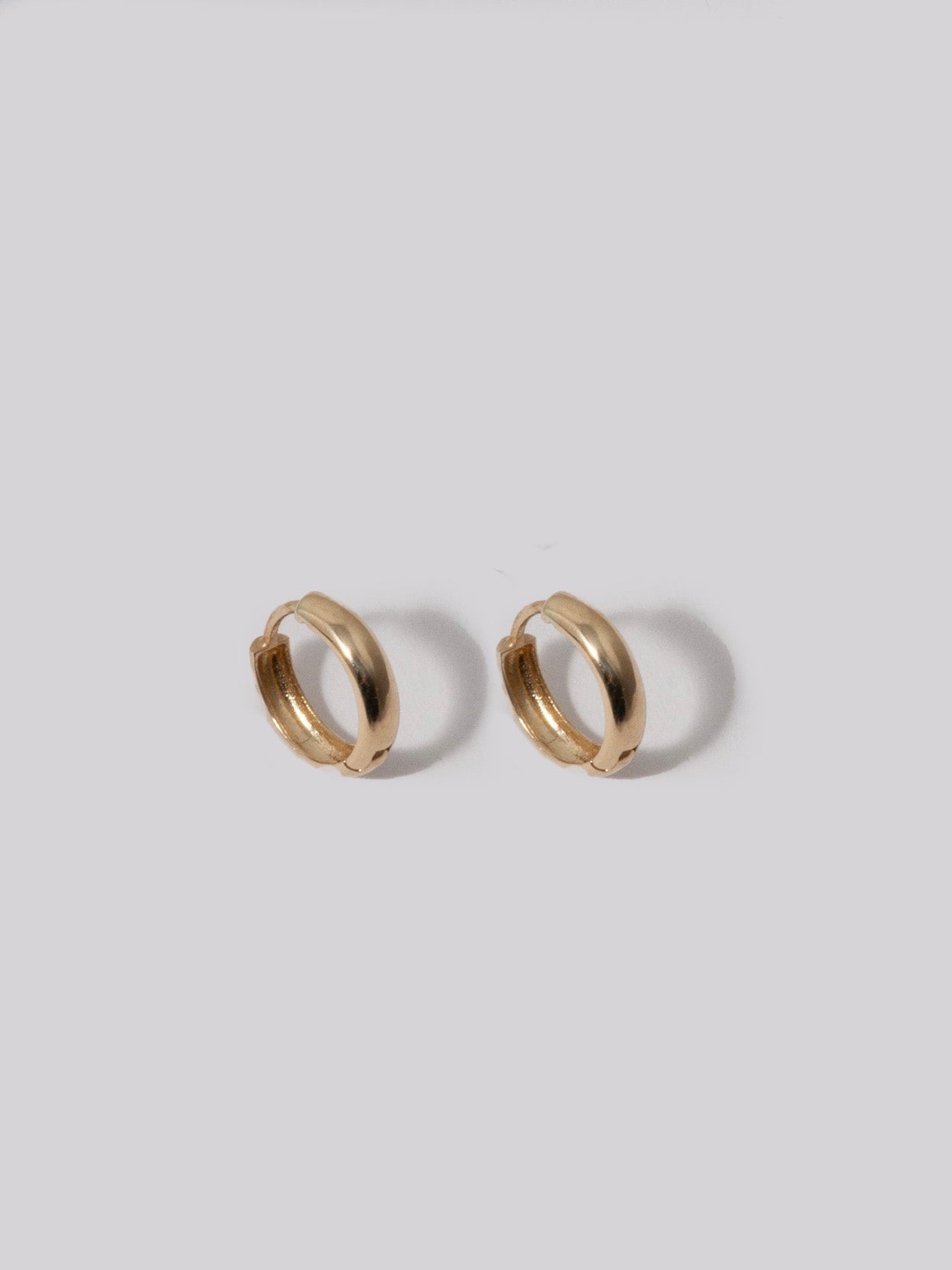 14kt Yellow Gold Anelli Huggies shot on light grey background.