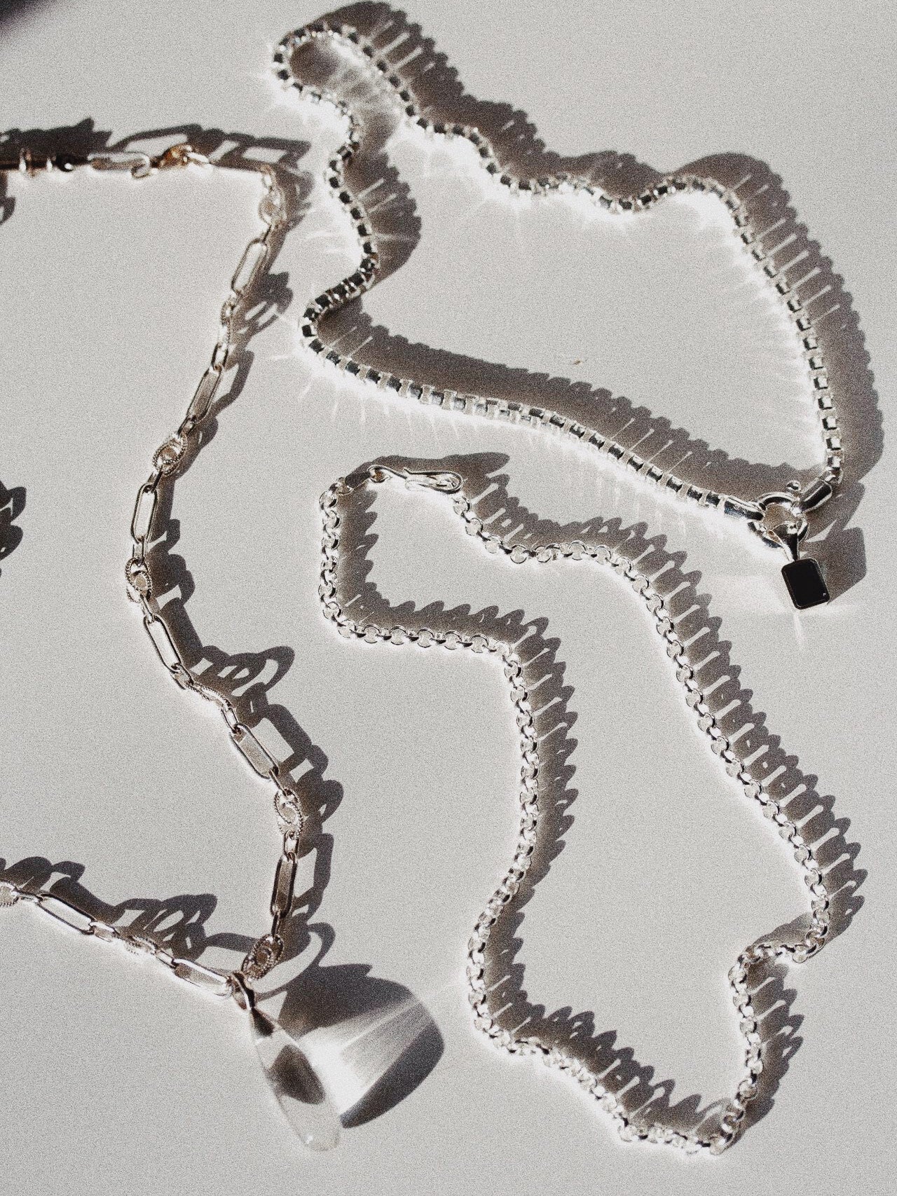 Sterling Silver Stone Teardrop Necklace pictured with the Sterling Silver Classic Rolo and the Cube Chain Choker with the Blue London Medallion Pendant. Light grey background. 