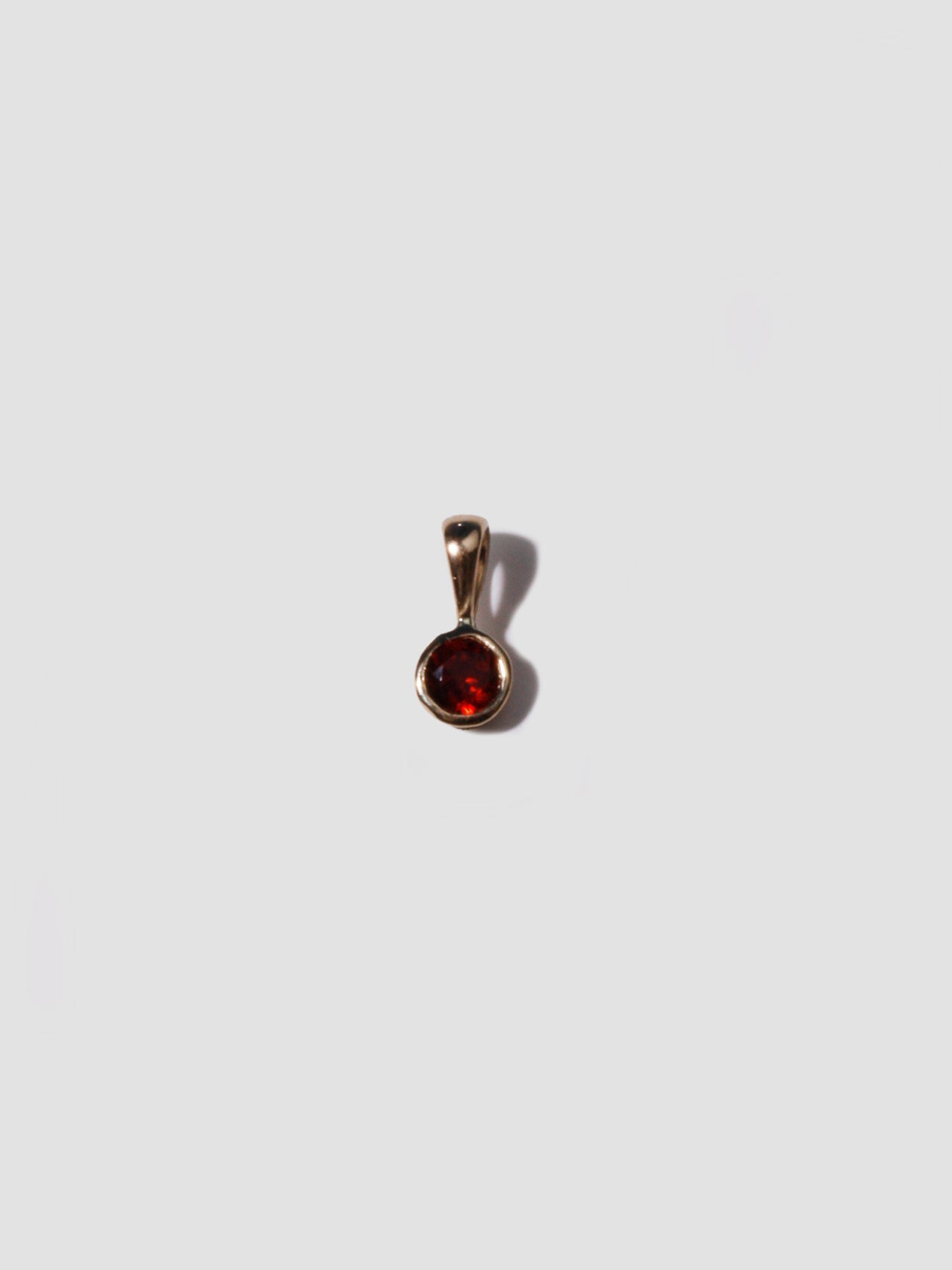 14kt Yellow Gold Garnet Bezel Charm pictured on light grey background. 