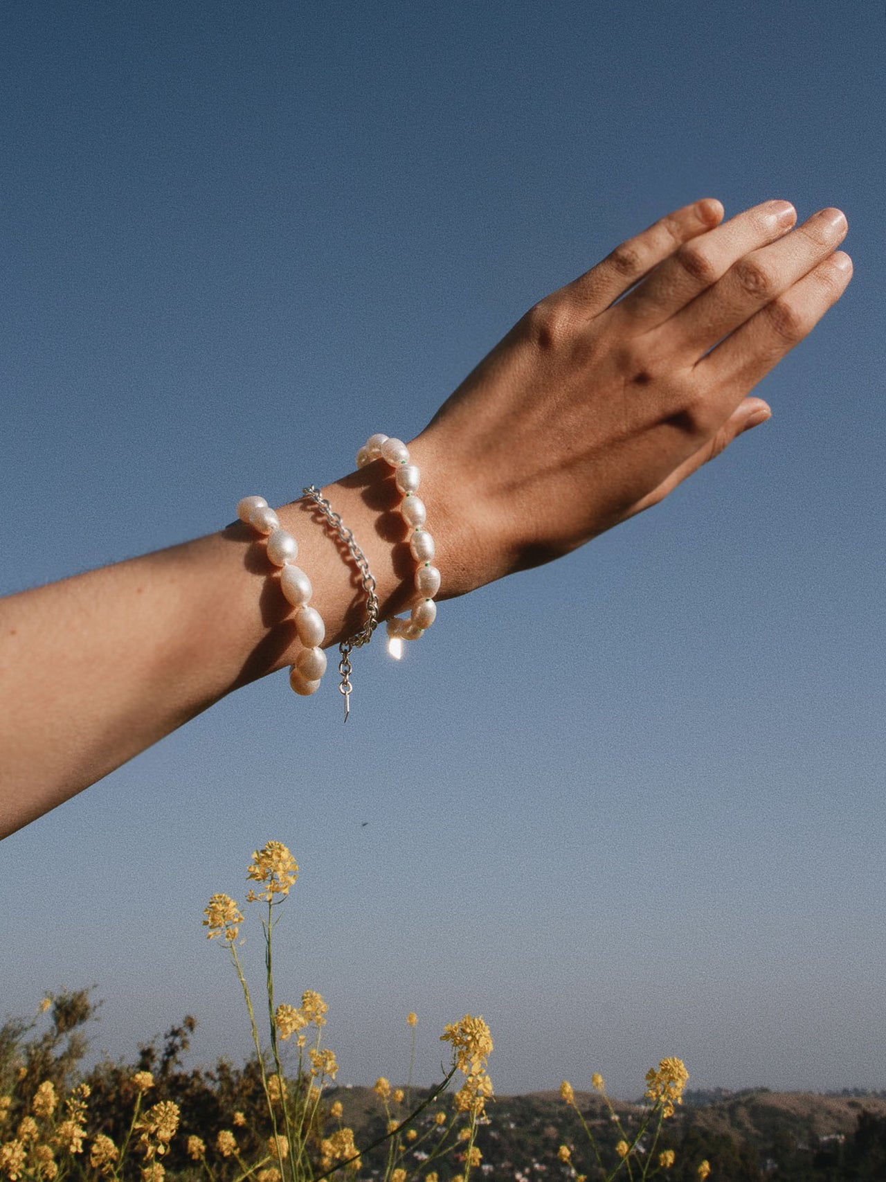 Sterling Silver Cable Chain Bracelet pictured on models wrist in between two pearl bracelets.