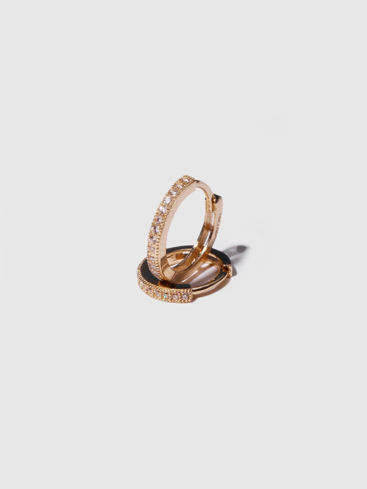 14kt Yellow Gold Pave Hoops pictured as pair on light grey background. One laying flat, other standing. 