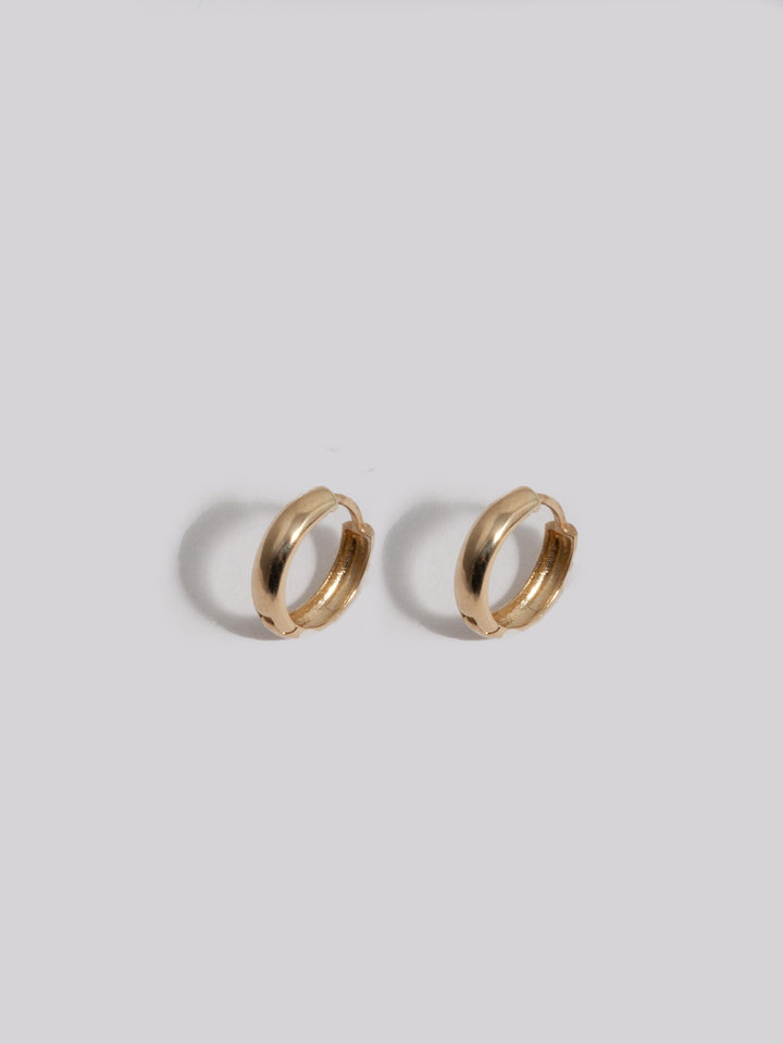 14kt Yellow Gold Anelli Huggies shot on light grey background.