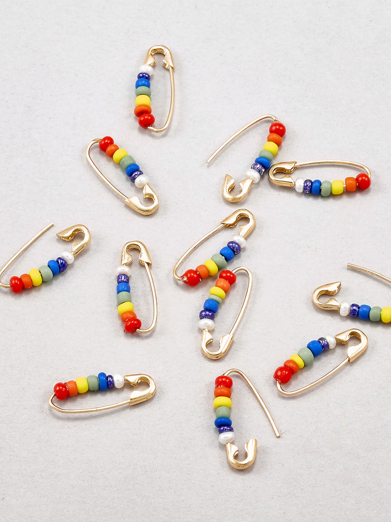 A handful of Pride Safety Pins spread out  and photographed on a light grey background.